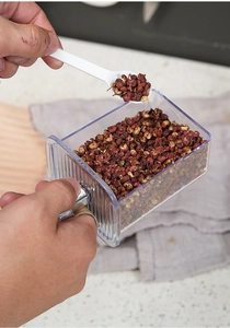 Close-up of clear wall-mounted spice box with pepper, metal handle and white spoon