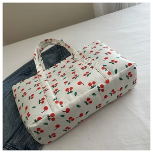 Detail of quilted cotton tote bag featuring red cherry prints on a bed background