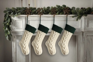 Close-up of four knitted Christmas stockings hanging on a white fireplace with pine decor