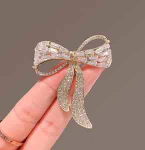Detailed close-up of a golden ribbon brooch featuring sparkling clear crystal rhinestones