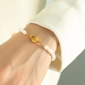 French retro natural pearl bracelet with a polished gold bean charm on a woman's wrist