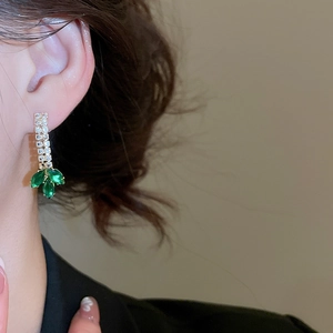 Close-up of elegant gold tassel earrings with green leaf gems and zircon on a model