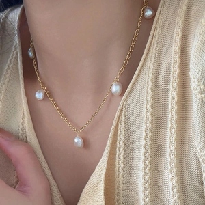 Close-up of woman wearing a gold chain necklace with five irregular baroque pearls