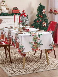 Detalle de mantel navideño con motivos de casas nevadas, pinos y campanas doradas festivas
