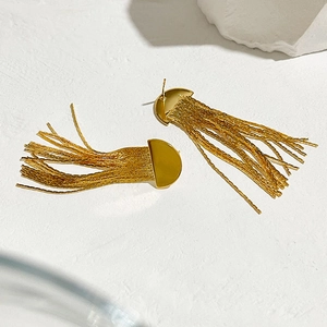 Détail de boucles d'oreilles dorées avec franges en chaîne serpent sur fond blanc texturé