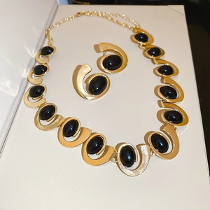 Detail view of geometric gold necklace and earrings set with black oval gemstones
