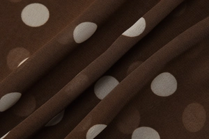 Gros plan d'un tissu mousseline marron à pois blancs montrant la texture lisse et fluide
