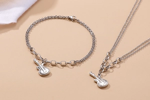 Detailed view of silver guitar pendant necklaces and bracelets on minimalist fabric