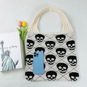 Macro view of knit tote bag with skull pattern and blue smartphone for size scale