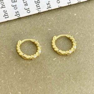 Close-up of golden twisted hoop earrings with sparkling cubic zirconia on a vintage paper