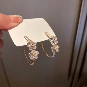 Detailansicht handgehaltener goldener C-Form Blumenohrringe mit funkelnden Strasssteinen