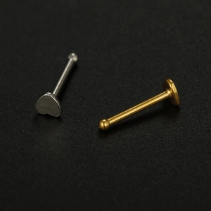 Macro view of gold ball and silver heart 20G stainless steel nose studs on textured background