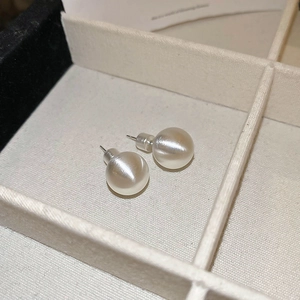 Detailed view of matte silver round stud earrings resting in a beige fabric jewelry box
