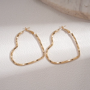 Close-up of golden heart-shaped earrings with a polished twisted design on stone