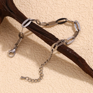 Silver stainless steel oval link chain anklet draped on a rustic branch background