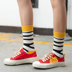 Street style low-top red canvas sneakers with yellow striped cotton crew socks on concrete