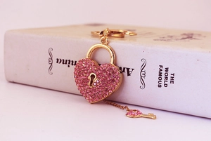 Macro detail of heart-shaped gold padlock keychain with pink rhinestones and a tiny key