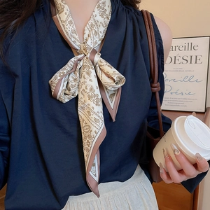 Detail of beige paisley printed silk scarf necklace worn with an elegant navy blue outfit
