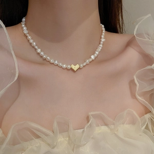 Close-up of pearl necklace with baroque pearls and textured gold heart pendant on neck