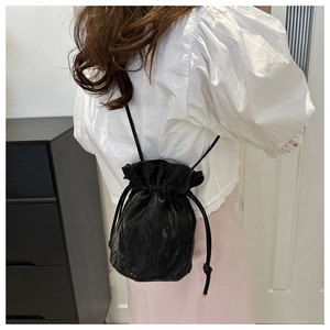 Detail of a black pleated bucket bag featuring a drawstring closure and a slender strap