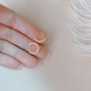 Elegant gold hoop earrings with small white pearls worn by a model on a neutral background