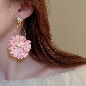 Close-up of pink fabric flower and pearl earrings worn by a model in soft lighting