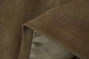 Detailed macro view showing the premium brown suede fabric and precise stitching of the jacket