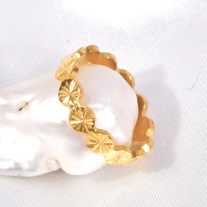 Detail of gold floral relief ring resting on a white pearl base with soft lighting