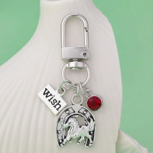 Silver metal keychain featuring horseshoe charm with horse pattern and a red rhinestone
