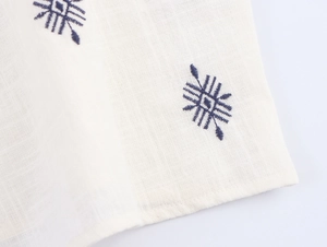 Detailed close-up of blue geometric embroidery on white linen cotton fabric texture