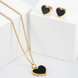 Elegant gold heart jewelry set with black stones on a white plush background