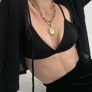 Detail of gold layered chain necklace with coin pendant on model in black mesh cardigan