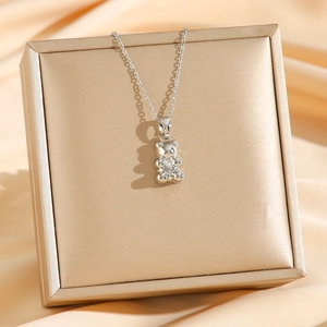 Minimalist silver teddy bear pendant necklace on a luxury champagne silk background