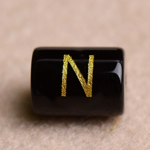 Detailed macro shot of a black cylindrical bead with a gold letter N for DIY jewelry