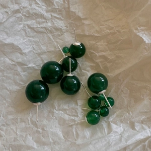 Detailed view of dark green agate bead earrings with silver pins on paper background