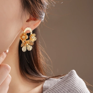 Close-up of golden oval pleated floral stud earrings with textured metal finish on ear