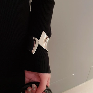 Dettaglio di un ampio bracciale rigido argento irregolare indossato sopra una manica nera