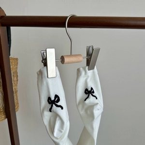 Detail of white cotton socks with black embroidered bows on a wooden hanger
