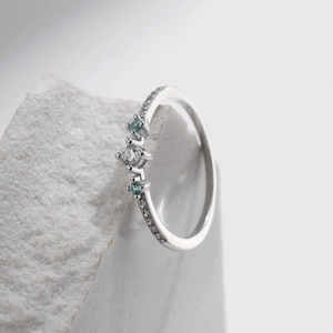 Elegant S925 sterling silver ring with central diamond and teal gemstones on a stone