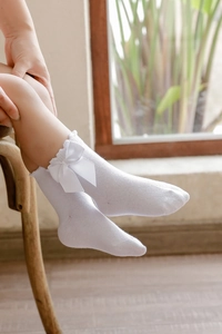 Close-up of white cotton girl socks with elegant silk bow and ruffled edges details