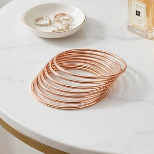 Detailed stack of rose gold minimalist round wire bangles on a marble background surface