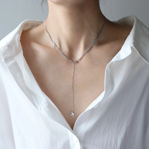 Détail du collier hirondelle argenté multicouche avec pendentif pompon sur le cou