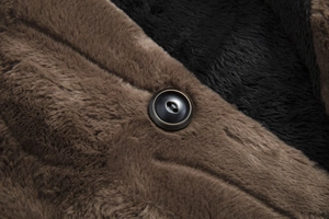 Detail of dark brown faux fur coat showing plush texture and a metallic rimmed button