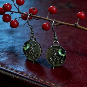 Detalle de pendientes vintage de bronce con relieve floral y gema verde oliva