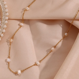 Detailed close-up of a gold chain necklace with white pearls on champagne silk fabric