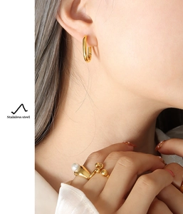 Detail of 18K gold-plated U-shaped earrings and pearl ring in stainless steel