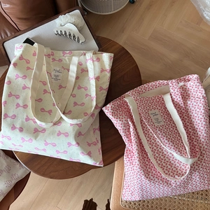 Détail de deux sacs cabas en toile avec imprimés nœuds roses et poignées en sangle renforcée