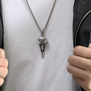 Detail shot of a silver raven skull pendant with Nordic runes on a model wearing a leather jacket