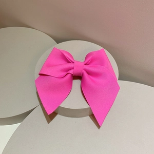 Detail of rose pink textured ribbon bow hair clip on a minimalist gray pedestal display