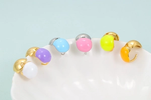 Close-up of six colorful enamel heart hoop earrings hanging on a white ceramic edge